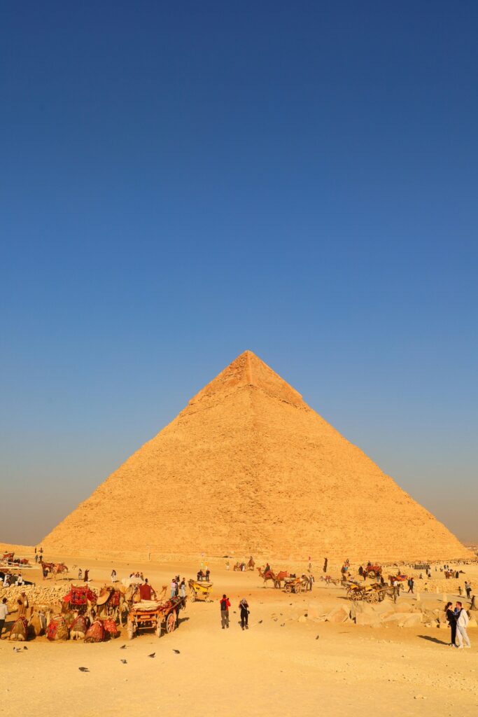 The iconic Great Pyramid of Giza with tourists and camels against a clear blue sky.